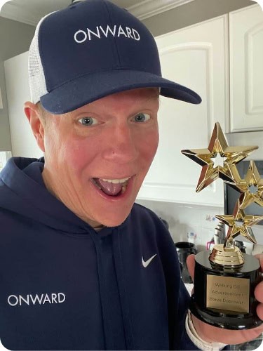 Man wearing Onward Search hat and hoodie holding up trophy for DEI